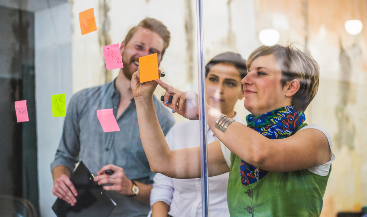 drei Personen kleben Post-Its auf eine Glasscheibe