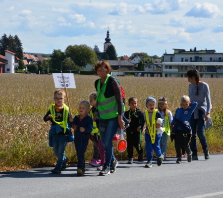 Eine Gruppe von Kindern gehen mit zwei Erwachsenen entlang eines Felds auf der Straße