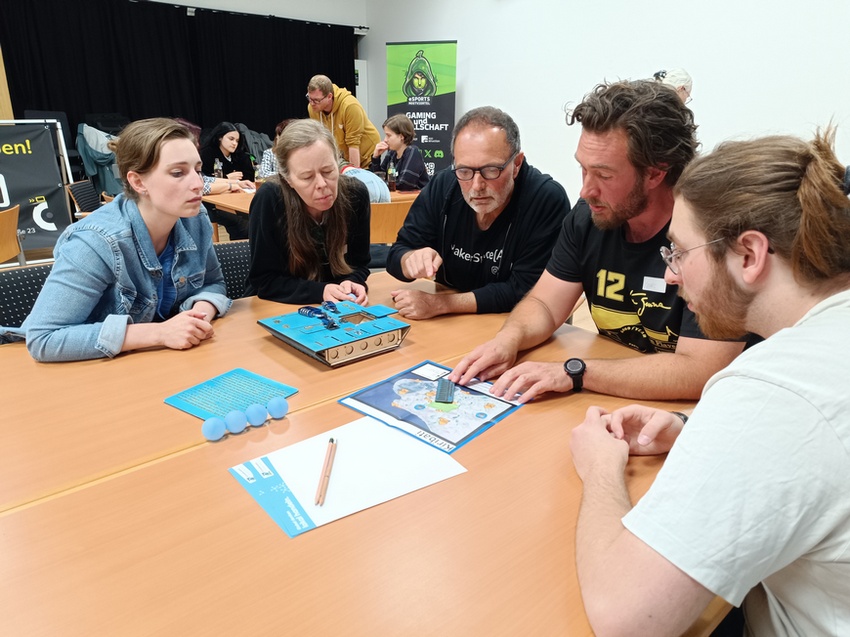 5 Menschen lösen gemeinsam Rätsel an einem Tisch.