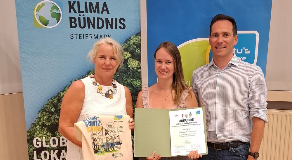 zwei Frauen und ein Mann mit Urkunde vor zwei Roll-Ups