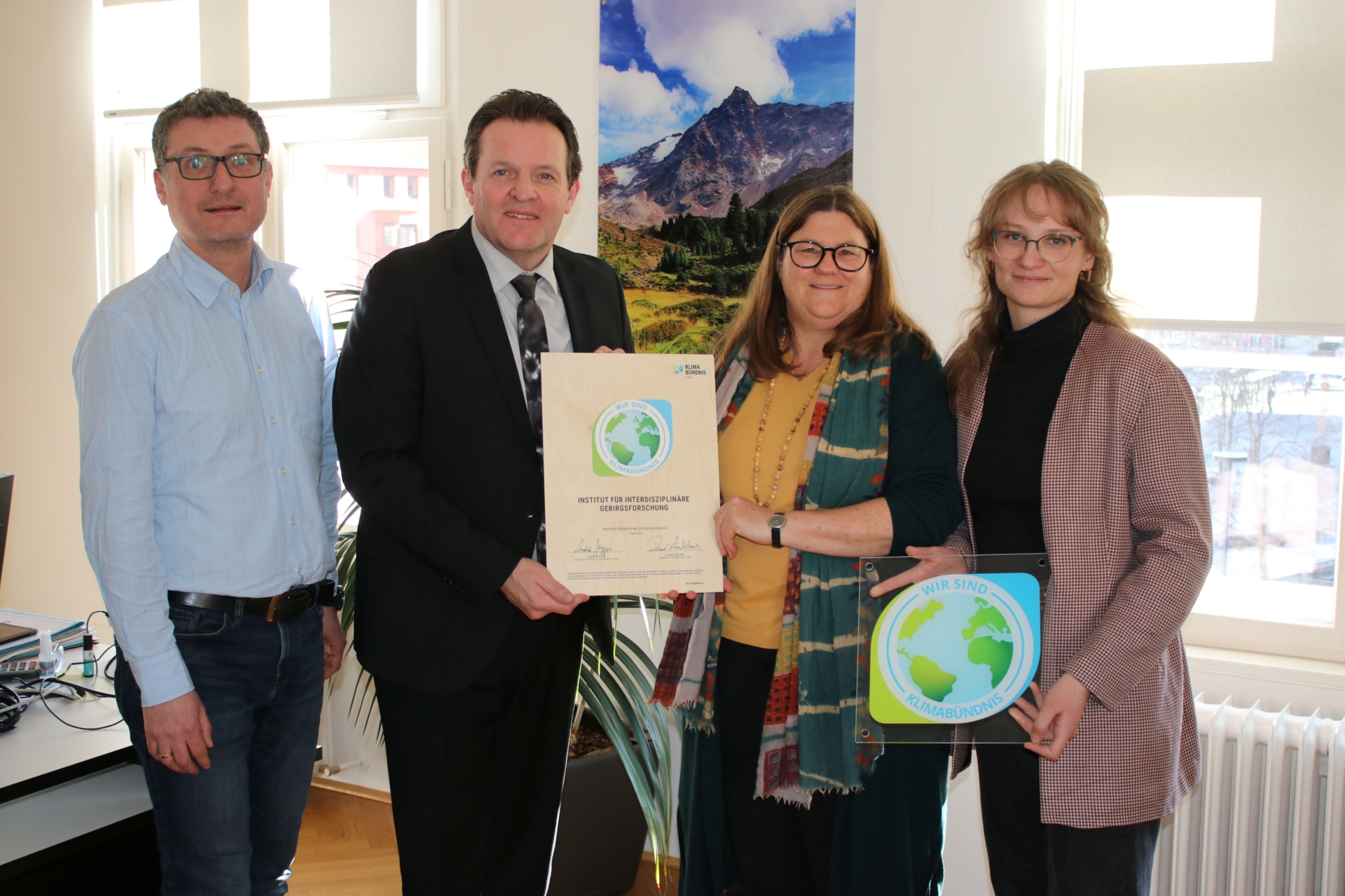 4 Personen lächeln in die Kamera und halten Klimabündnisurkunde und Tafel hoch