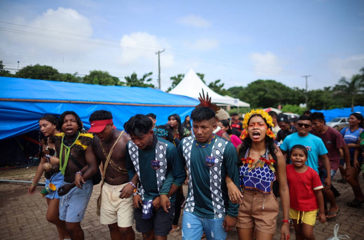 Indigene stehen mit den Armen untergesagt in Reihen und rufen etwas