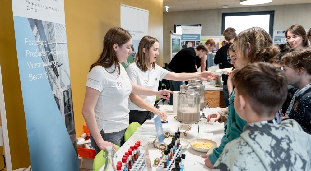 Kinder schauen sich interessiert einen Info-Stand zu einer HBLFA an