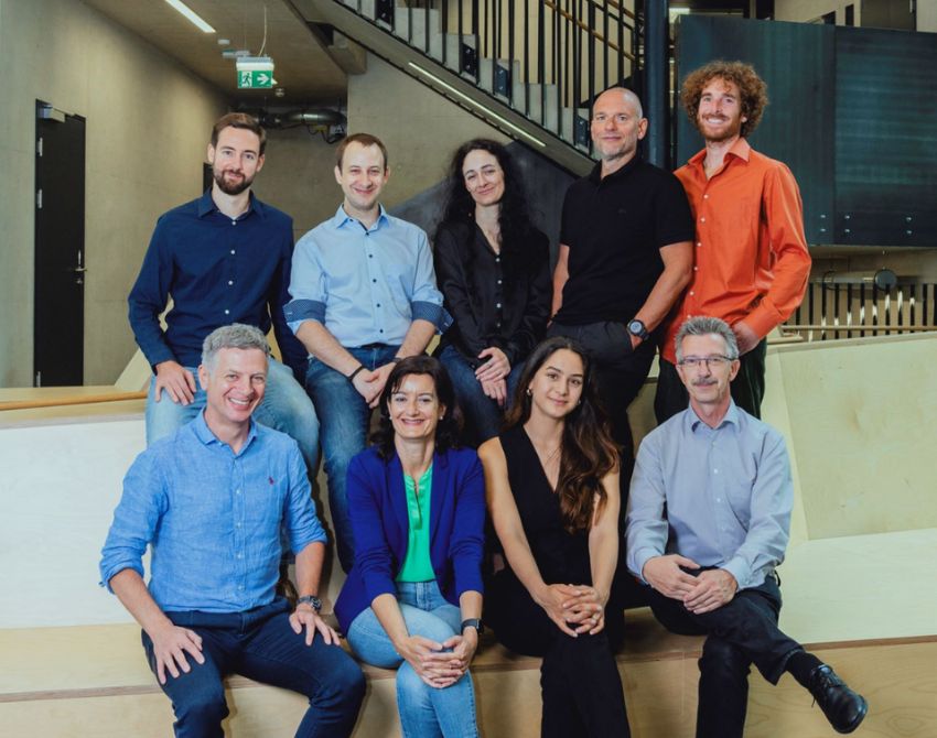 Gruppenbild von neun Personen, vier sitzen, vier stehen mittleren alters business casual