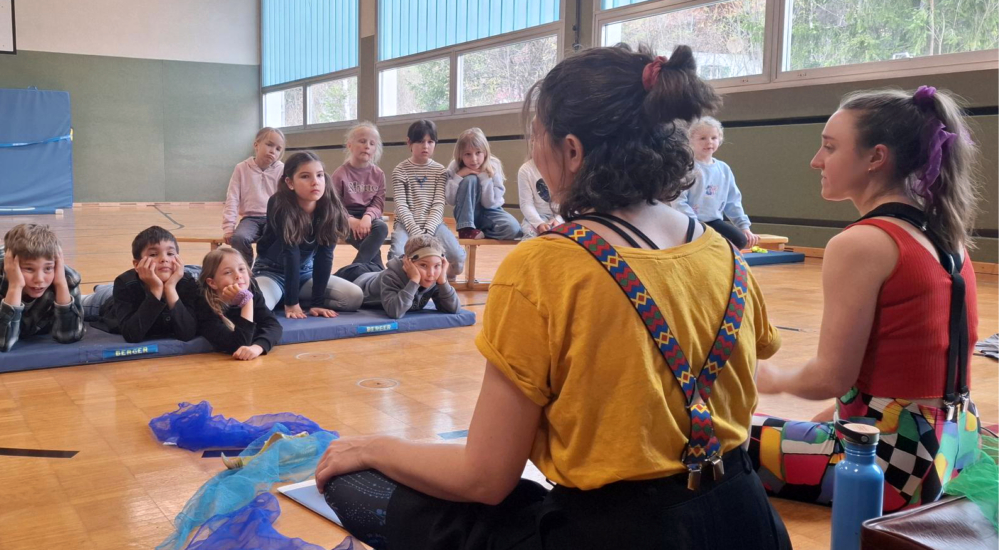 Kinder sitzen im Halbkreis um die Pädagoginnen des Klimazirkus