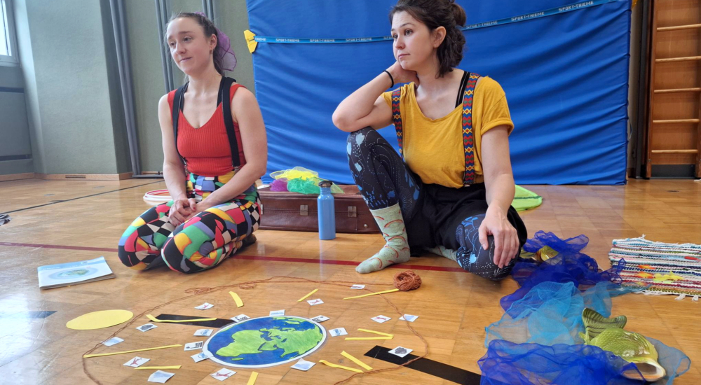 Zwei Pädagoginnen des Klimazirkus sitzen im Turnsaal mit Erde zur Erklärung des Treibhauseffekts