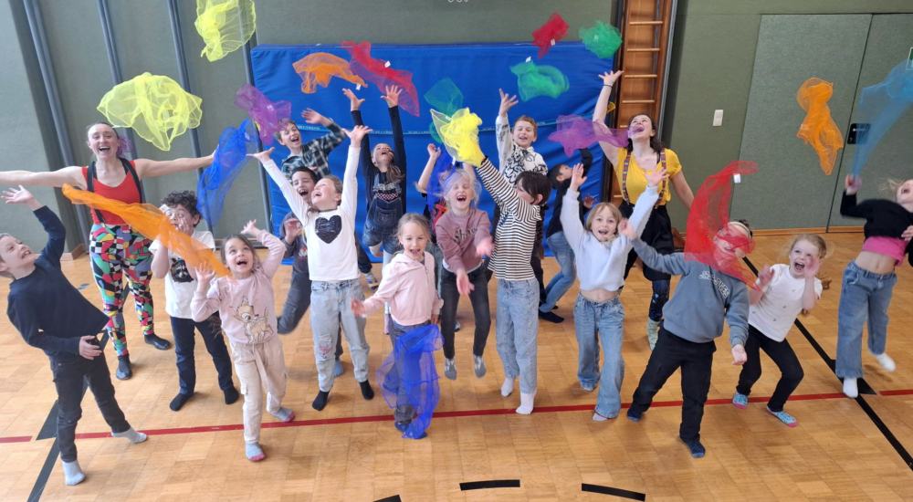 Kinder springen glücklich in die Luft und werfen dabei bunte Tücher in die Luft