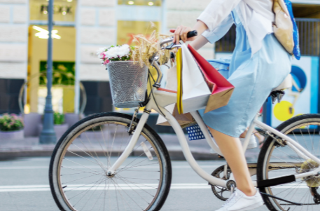 Frau am Rad mit Blumen im Korb und Einkaufstaschen