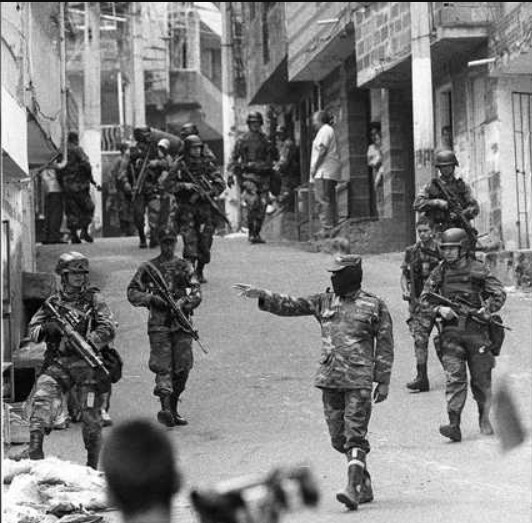 Operation Orion in der Comuna 13 von Medellín. Oktober 2002. Auf dem Foto ist ein paramilitärischer Anführer zu sehen, der dem Militär bei der Einnahme der Comuna 13 in Medellín Befehle erteilt. Bis heute gelten mehr als 150 Menschen als verschwunden, und der Staat wurde wegen dieses Massakers verurteilt. Foto: Jesus Abad Colorado.